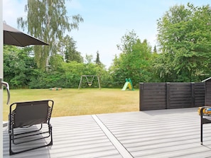 A deck with a swing set and a slide in the background.