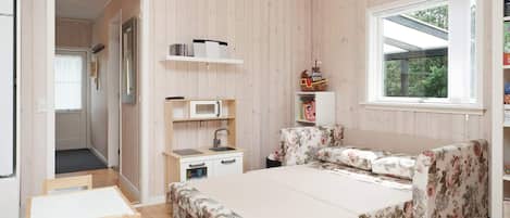 A bedroom with a bed, a desk, a chair, a small kitchenette, and a window.