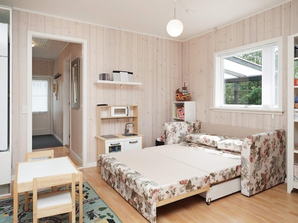 A bedroom with a bed, a desk, a chair, a small kitchenette, and a window.