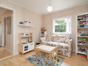 A cozy room with a wooden floor, a floral sofa, a small table, a bookshelf, and a window with a view of greenery.