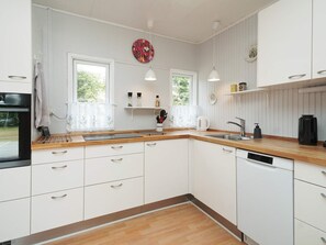A modern kitchen with white cabinets, a wooden countertop, a built-in oven, and a window with a view of greenery. - 6 Person Holiday Home in Hojby (Hojby)