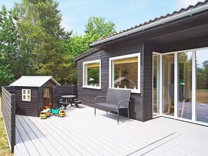 Een houten terras met een kleine speelruimte, een tafel en stoelen.