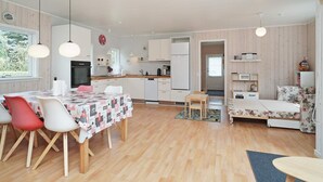 A modern kitchen with white cabinets, a dining area with a table and chairs, and a living space with a sofa and a small table. - 6 Person Holiday Home in Hojby (Hojby)
