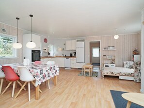 A modern kitchen with white cabinets, a dining area with a table and chairs, and a living space with a sofa and a small table. - 6 Person Holiday Home in Hojby (Hojby)