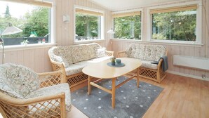 A cozy room with a round wooden table, two patterned sofas, wicker chairs, and large windows with blinds. - 6 Person Holiday Home in Hojby (Hojby)