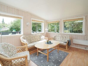 A cozy room with a round wooden table, two patterned sofas, wicker chairs, and large windows with blinds. - 6 Person Holiday Home in Hojby (Hojby)