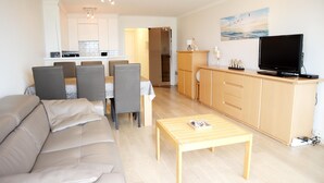A modern living room with a sofa, dining table, and chairs. There is a kitchen area with cabinets and a television. - Apartment in Nieuwpoort Near the Beach (Nieuwpoort)