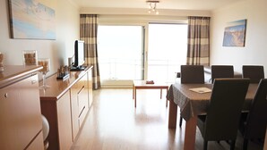 A modern hotel room with a dining area, a TV, and a balcony with curtains. - Apartment in Nieuwpoort Near the Beach (Nieuwpoort)