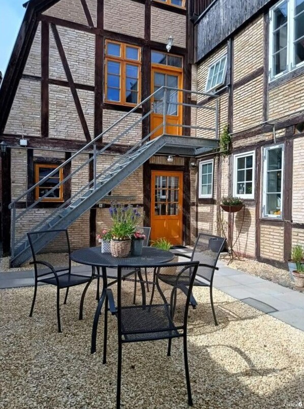 A traditional half-timbered building with a staircase leading to the entrance, a round table with chairs, and potted plants. - De Bohn Comfortable Holiday Residence (Lübeck)