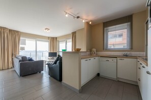 Um apartamento moderno com sala de estar, cozinha compacta e grandes janelas.