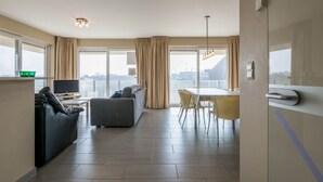 Et moderne hotelværelse med opholdsområde, spiseplads og store vinduer med udsigt over byen.