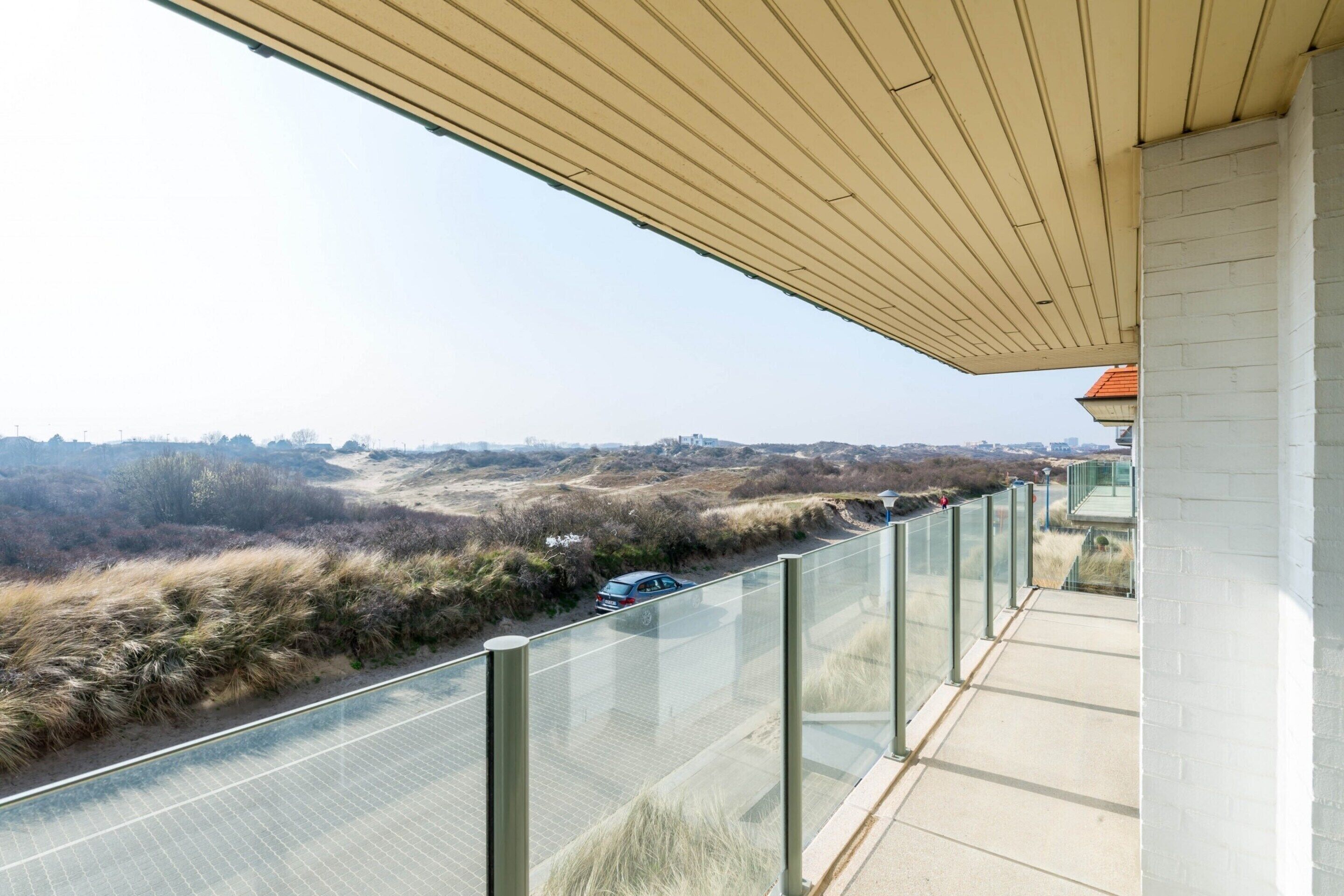 A balcony with a glass railing overlooking a road and distant landscape.
