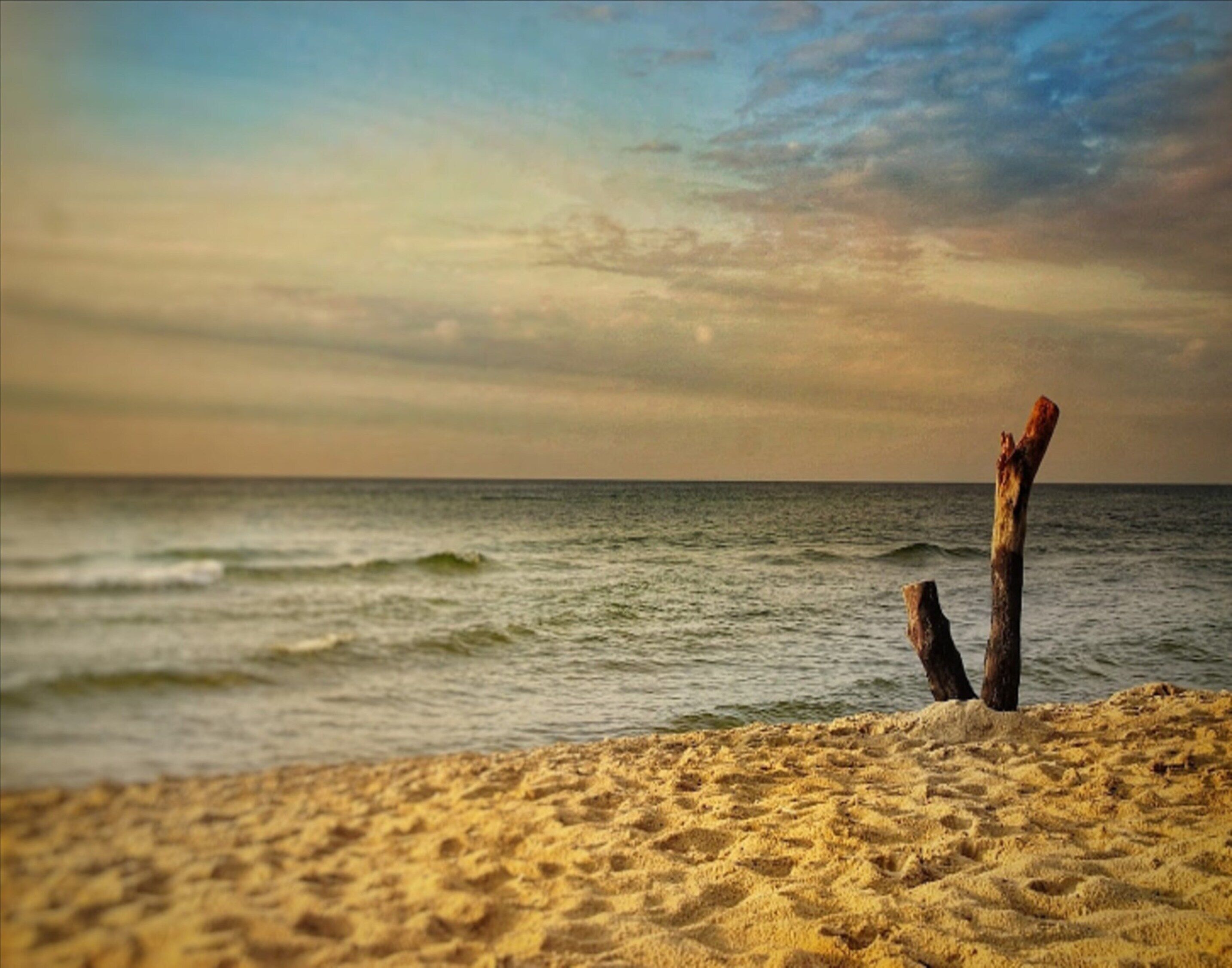 A beach scene with a wooden post in the sand and waves in the background.