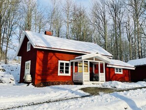 A red wooden house with a snow-covered roof and a porch.