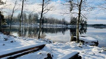 A snow-covered landscape with a calm lake, trees, and a wooden dock.