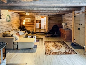 A cozy log cabin interior with a sofa, armchairs, a fireplace, and a rug.