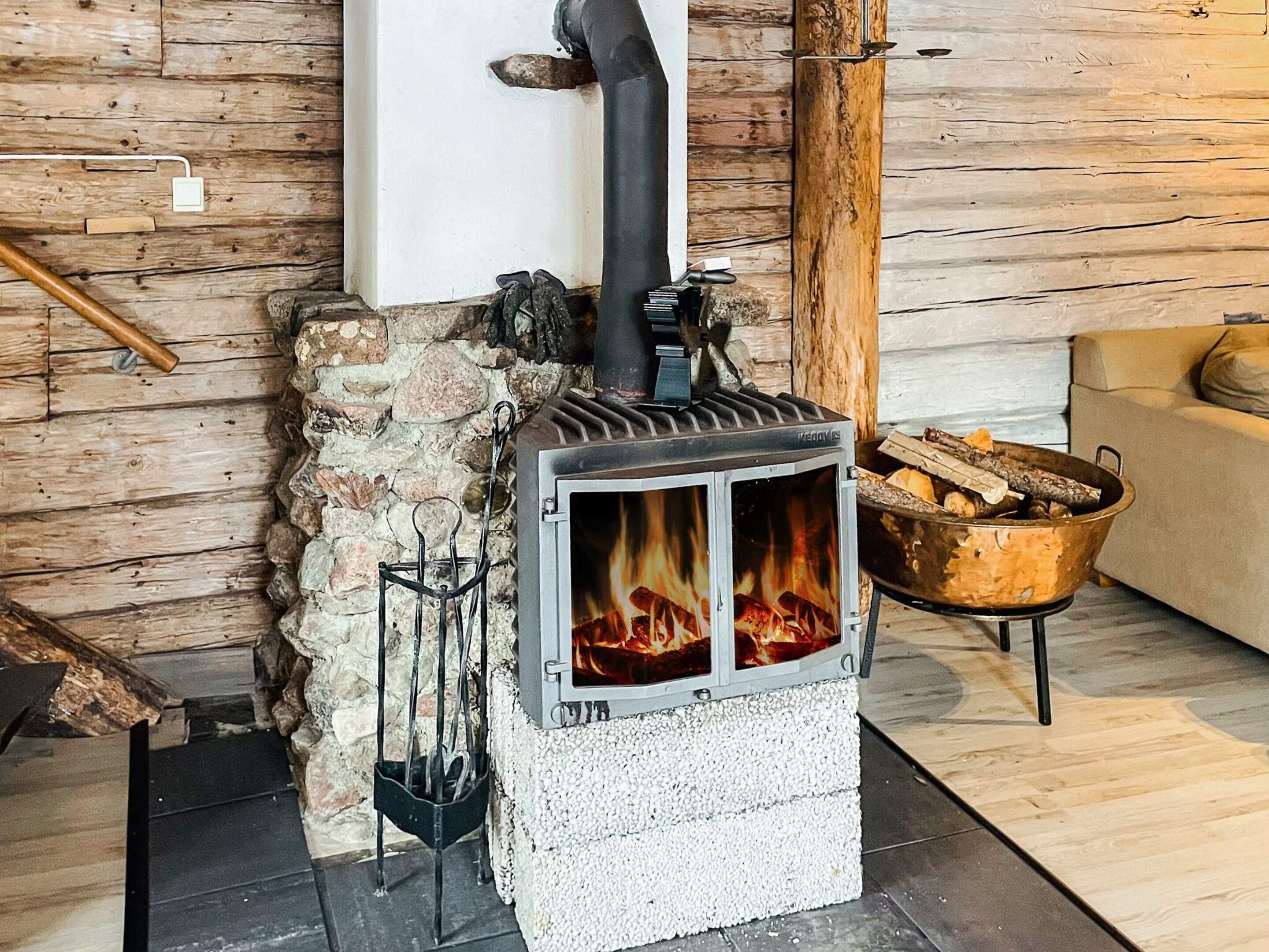 A wood-burning stove with a stone wall and a log holder nearby.