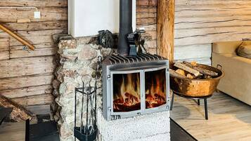 A wood-burning stove with a stone wall and a log holder nearby.