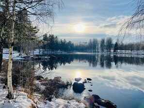 A serene winter landscape with a calm lake reflecting the sky and trees, surrounded by snow-covered ground and bare trees. - 4 Person Holiday Home in Aseda (Åseda)