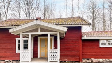 A red wooden house with a white porch and a yellow door.