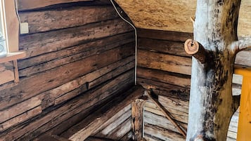 A log cabin interior with wooden walls, a wooden floor, and a central wooden beam structure.