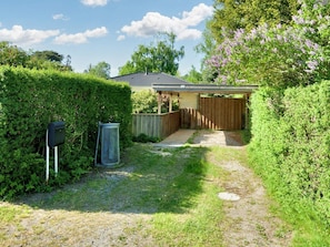 A covered outdoor area with a wooden fence, a metal trash bin, and a pathway leading to a building. - 6 Person Holiday Home in Gilleleje (Gilleleje)