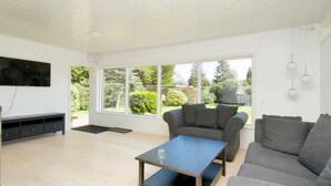 A spacious living room with a large window, a flat-screen TV, a grey sofa, and a coffee table. - 6 Person Holiday Home in Gilleleje (Gilleleje)
