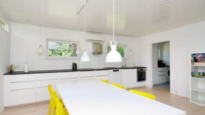 A modern kitchen with white cabinets, a black countertop, and a white dining table with yellow chairs. There are pendant lights above the table and a window with a view of greenery outside. - 6 Person Holiday Home in Gilleleje (Gilleleje)