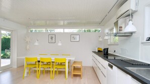 A modern kitchen with white cabinets, a black countertop, and a wooden dining table with yellow chairs. - 6 Person Holiday Home in Gilleleje (Gilleleje)