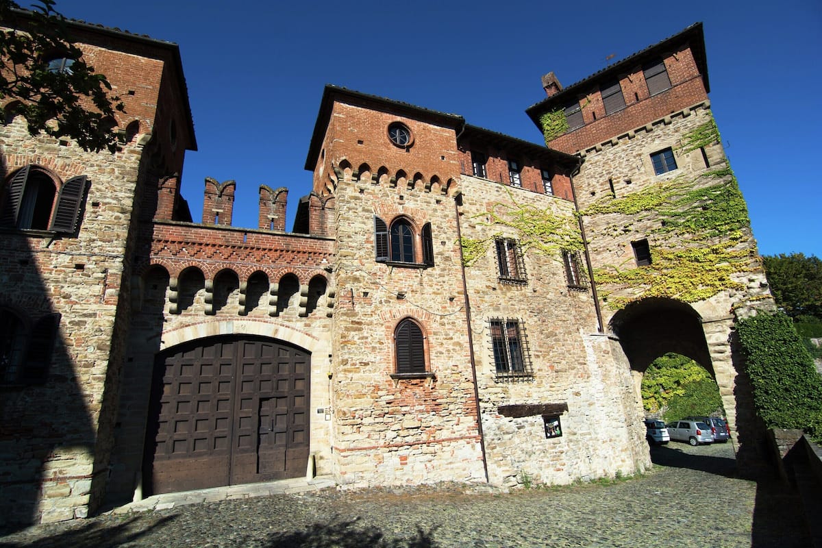 Un edificio histórico de piedra con arcos en puertas y ventanas, una torre de reloj y muros cubiertos de hiedra.