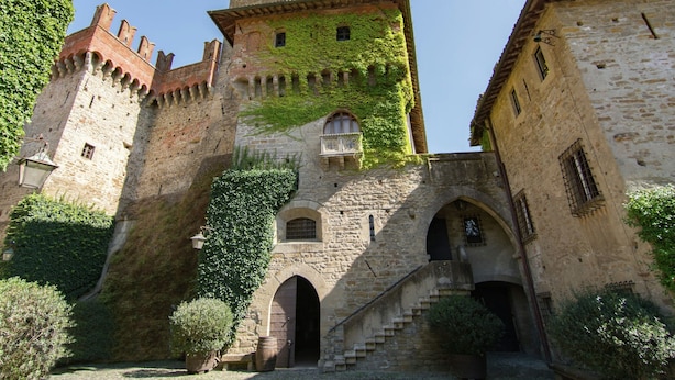 Un château de pierre historique, doté d’une tour, d’une entrée en arc de cercle et de murs couverts de lierre.