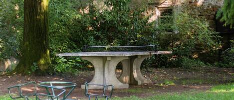 Una mesa de piedra con sillas en un jardín, con un árbol y un muro de piedra al fondo.