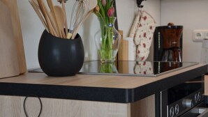 A kitchen counter with a black bowl containing wooden utensils, a glass vase with flowers, and a coffee machine. - Pleasant Apartment in Stadtilm (Stadtilm)