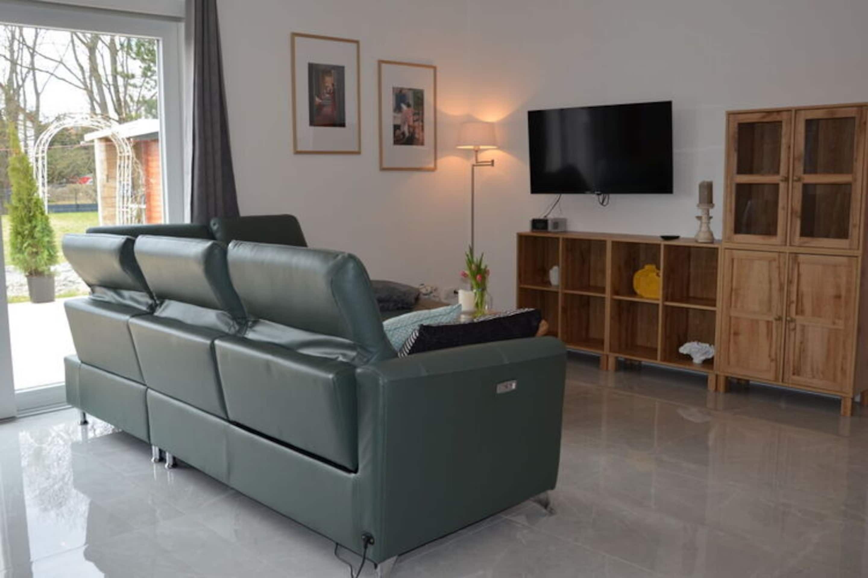 Ein modernes Wohnzimmer mit einem grünen Sofa, einem Flachbildfernseher, einem Holzschrank und einer Stehlampe.