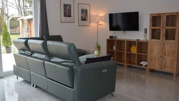 Ein modernes Wohnzimmer mit einem grünen Sofa, einem Flachbildfernseher, einem Holzschrank und einer Stehlampe.