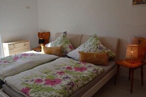 Een slaapkamer met een bed, nachtkastje, stoel en lamp.