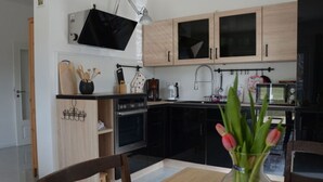 A modern kitchen with wooden cabinets, a black countertop, and a dining area with a table and chairs. - Pleasant Apartment in Stadtilm (Stadtilm)