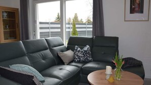 A modern living room with a dark green leather sofa, a round wooden coffee table, and a glass cabinet. - Pleasant Apartment in Stadtilm (Stadtilm)