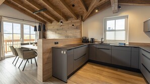 Eine moderne Küche mit Holzbalken, einem großen Fenster und einer Essecke mit Stühlen.