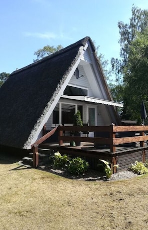 Una casa con techo de paja, terraza de madera y un pequeño porche.