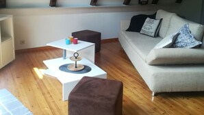 A modern living room with a sofa, a coffee table, and a side table. There is a wooden floor and a sloped ceiling with exposed beams. - \"the Elf\" Comfortable Holiday Residence (Gartow)
