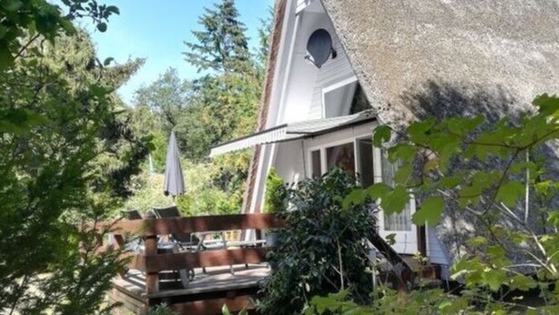 A house with a thatched roof, a wooden deck, and a garden with various plants. - \"the Elf\" Comfortable Holiday Residence (Gartow)