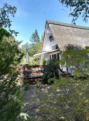 Ein Haus mit Strohdach, einer Holzterrasse und einem Garten mit verschiedenen Pflanzen.