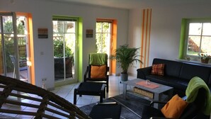 A living room with a sofa, chairs, a coffee table, and a potted plant. There are two doors leading to an outdoor area. - Nordgluck Modern Retreat (Taarstedt)