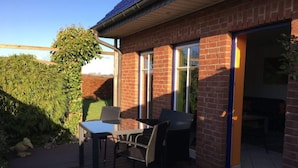 A patio with a table and chairs, a brick building, and a sliding glass door leading to an interior space. - Nordgluck Modern Retreat (Taarstedt)