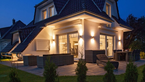 Ein zweistöckiges Haus mit geneigtem Dach, einer überdachten Terrasse und einem gut beleuchteten Eingang.