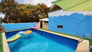 A swimming pool with a blue and white wall, surrounded by a fence and trees with orange flowers. - Belvilla by OYO Casa Tata (Granadilla de Abona)