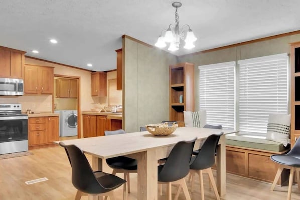 Cocina compacta con armarios de madera, horno integrado y comedor con mesa y sillas.