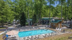 A swimming pool with lounge chairs and a small building, surrounded by trees.