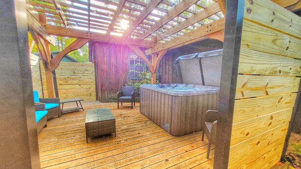 An outdoor deck with a hot tub, seating area, and wooden pergola.
